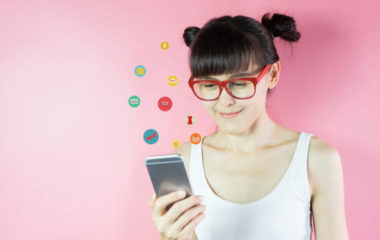 Young woman using smartphone with shopping icons flying around on pink background